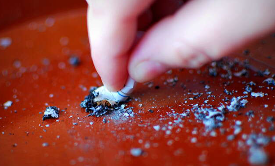 A hand crushes the tip of a cigarette on a red counter