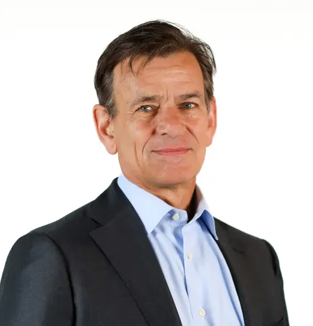 A man with dark hair wears a grey suit jacket and light blue button down.