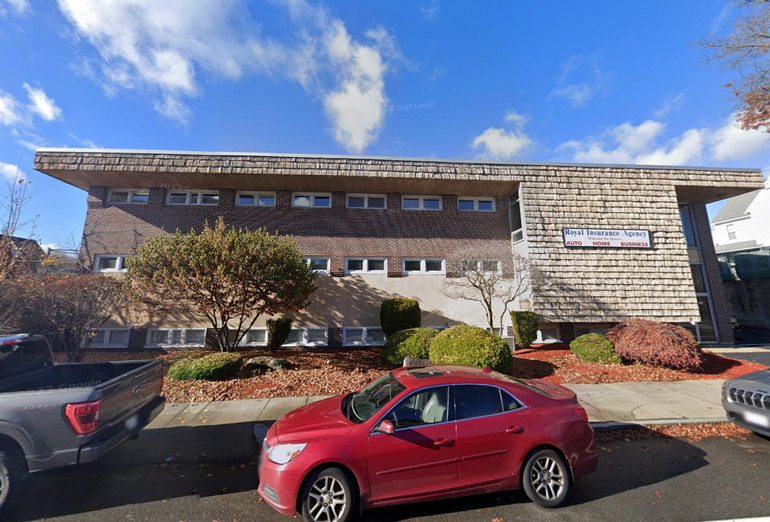 A three-story office building with a brick and shingle facade sits behind parked cars on a street