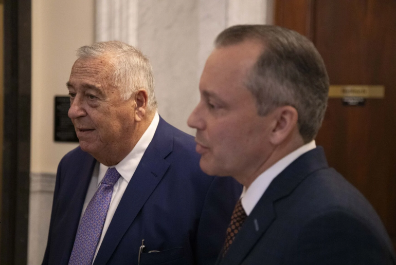 Man in a suit stands next to another man in a suit