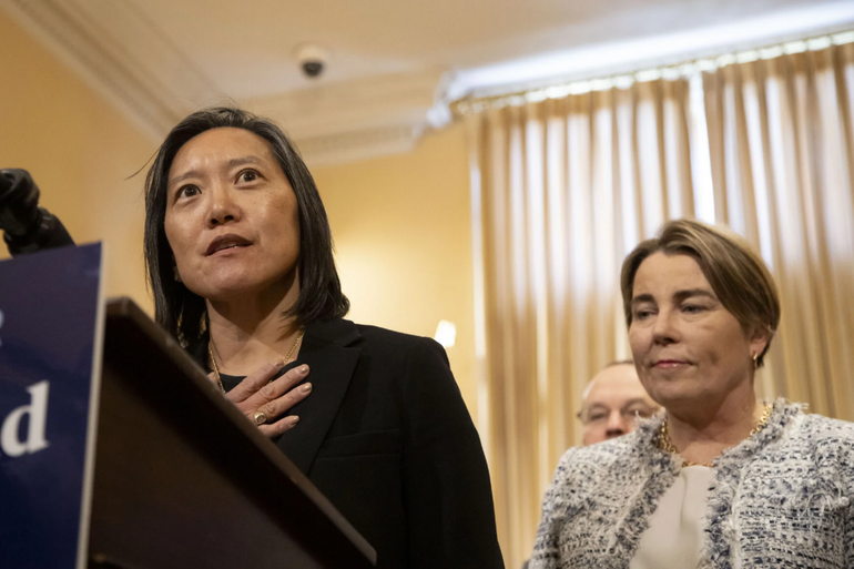 A woman stands at a podium flanked by another woman