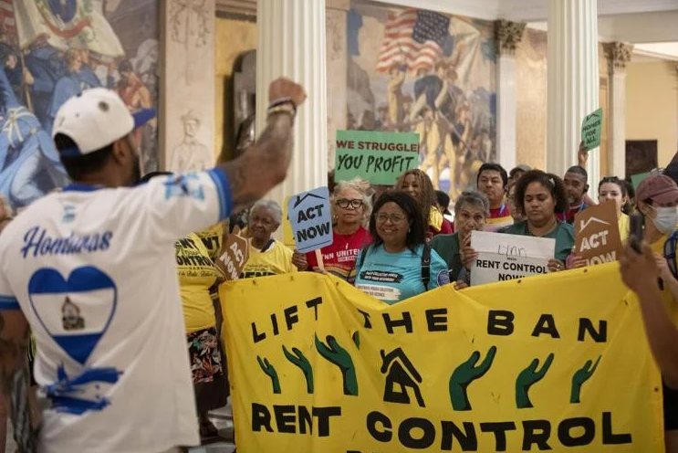 Group of protestors with banners and signs about rent prices and rent control gather in the statehouse