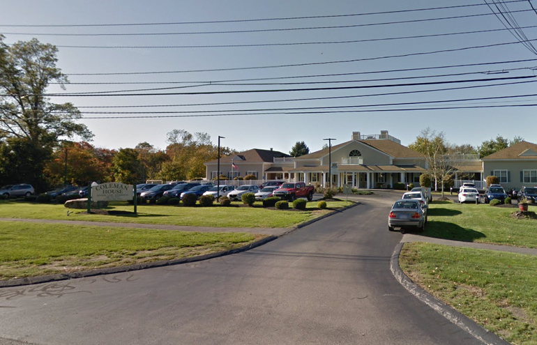 A one-story building sits behind a lawn and parking lot