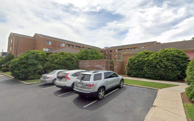 Exterior of a three-story brick hotel building with parking in front