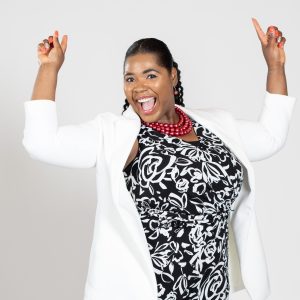 A woman wears a white jacket over a black flower-print dress.
