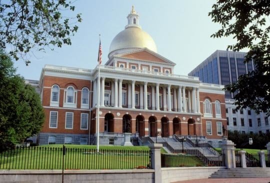 A large brick building with columns in front and a gold dome on top with a long staircase leading up to it and an American flag on the left hand side.