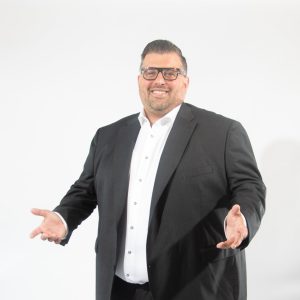 A man in a black suit smiles and shrugs