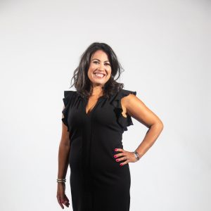 A woman in a black dress with a hand on hip smiles
