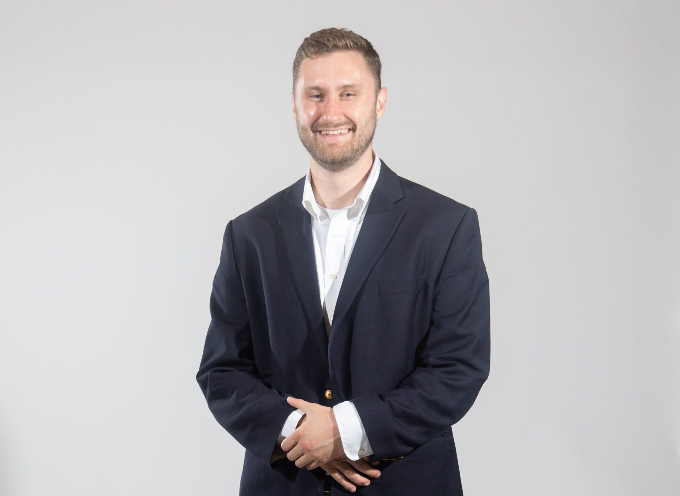 A man wears a black suit jacket, a white button down, and tan pants.