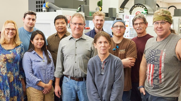 A group of people pose for a photo in a machine shop.