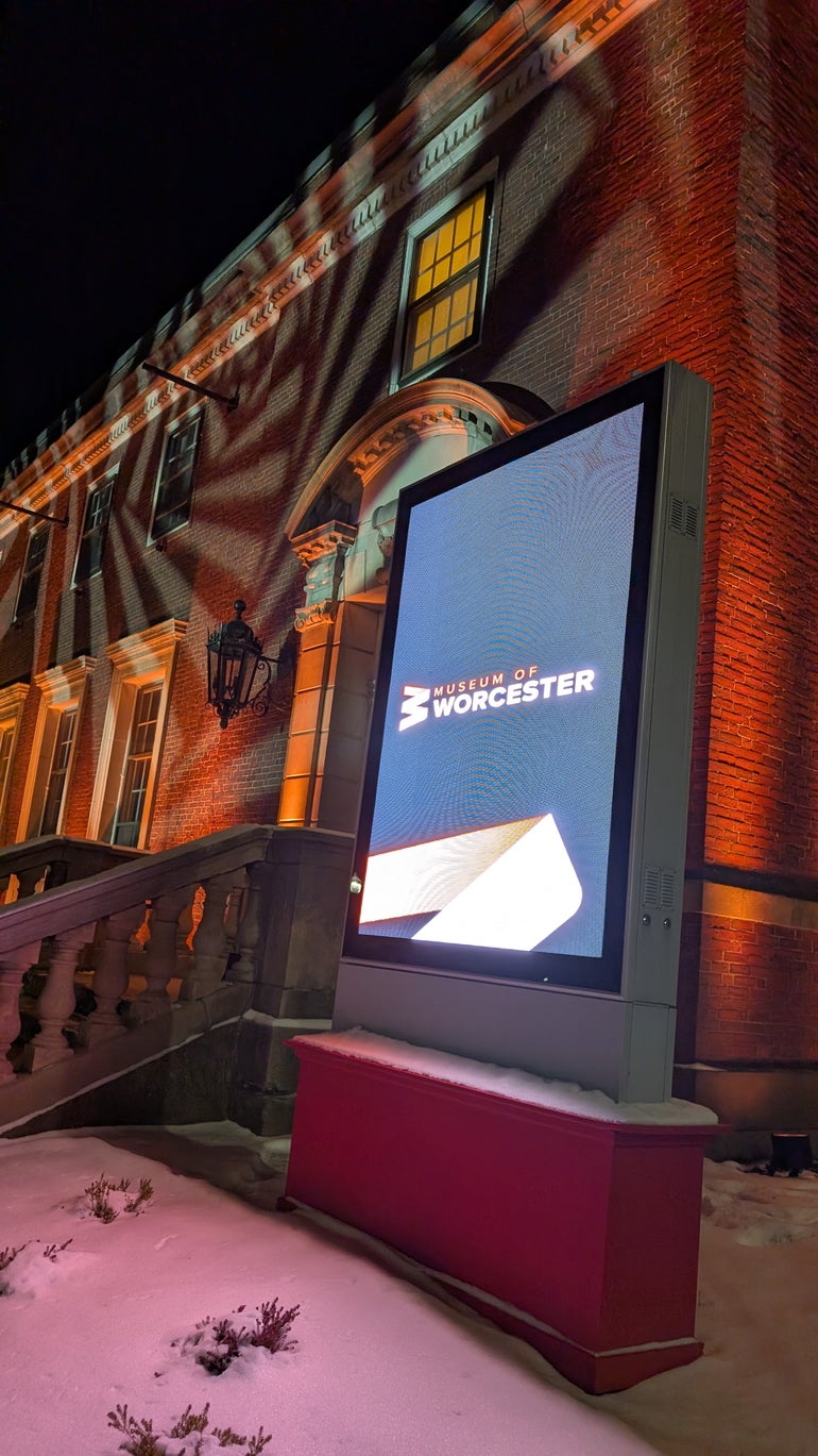 Outside a brick museum lit by patterned lights with a digital sign in front of it reading 
