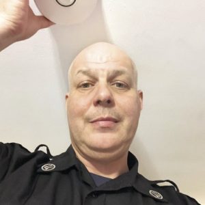 A man wearing a black uniform holds a fire alarm to a ceiling.