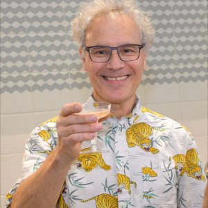 Man in dress shirt with tigers and leafs on it smiles while holding  a martini glass