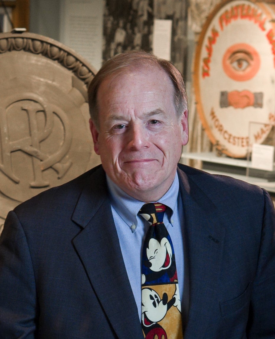 A man wears a dark blue blazer, light blue button down, and a Mickey Mouse tie.
