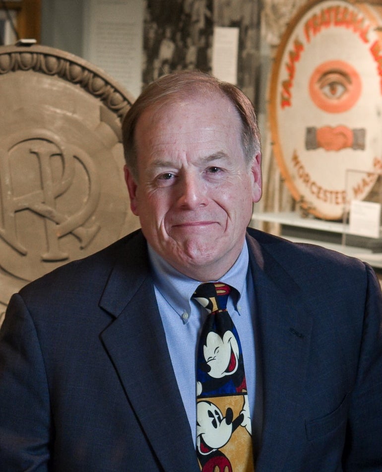 A man wears a dark blue blazer, light blue button down, and a Mickey Mouse tie.