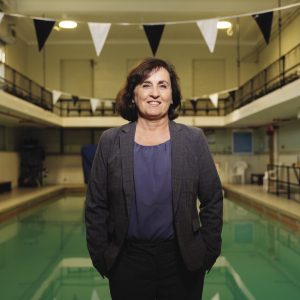 A woman wearing a grey suit stands in front of an indoor pool.