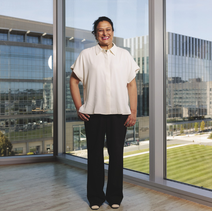 A woman stands in front of windows overlooking a college campus.