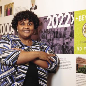 A woman leans against a wall with posters on it.