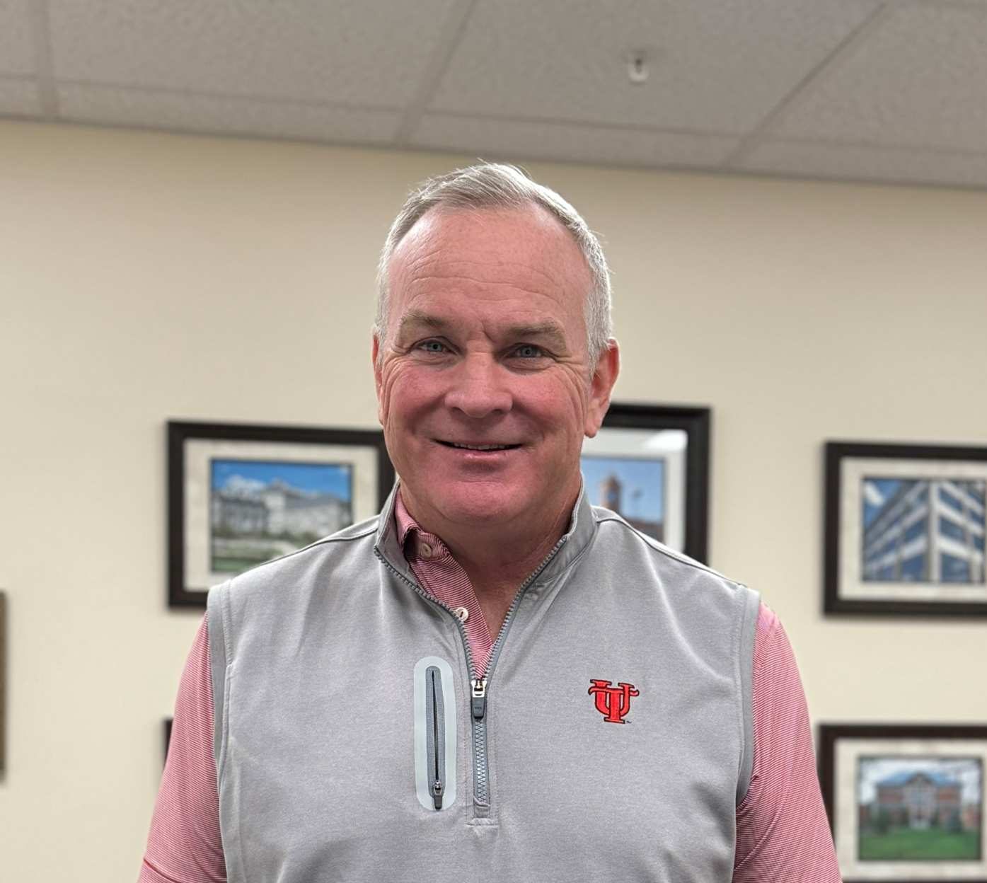 Man in vest with short sleeve shirt underneath poses for photo in office