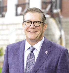 A man wears black glasses and a blue suit jacket.
