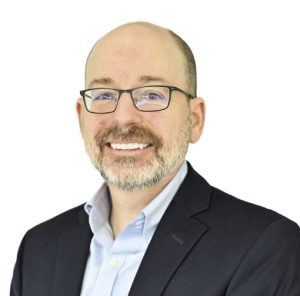 A man wears a black blazer and light blue button down.