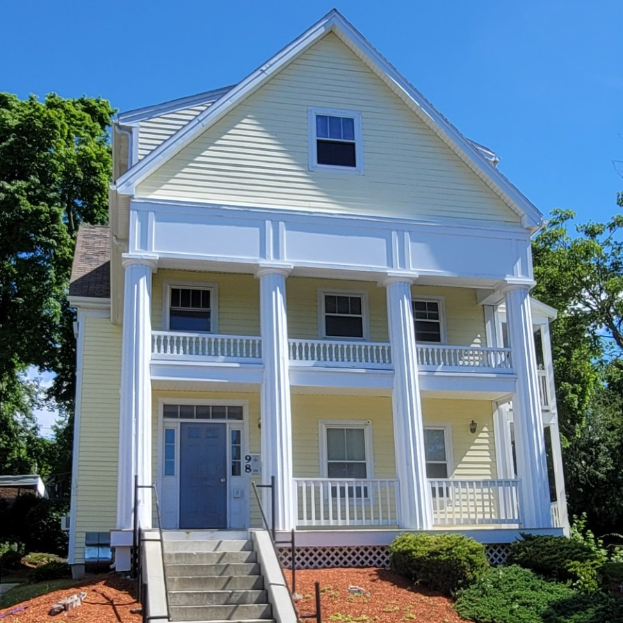 A three-story, yellow residential building with a porch and white columns