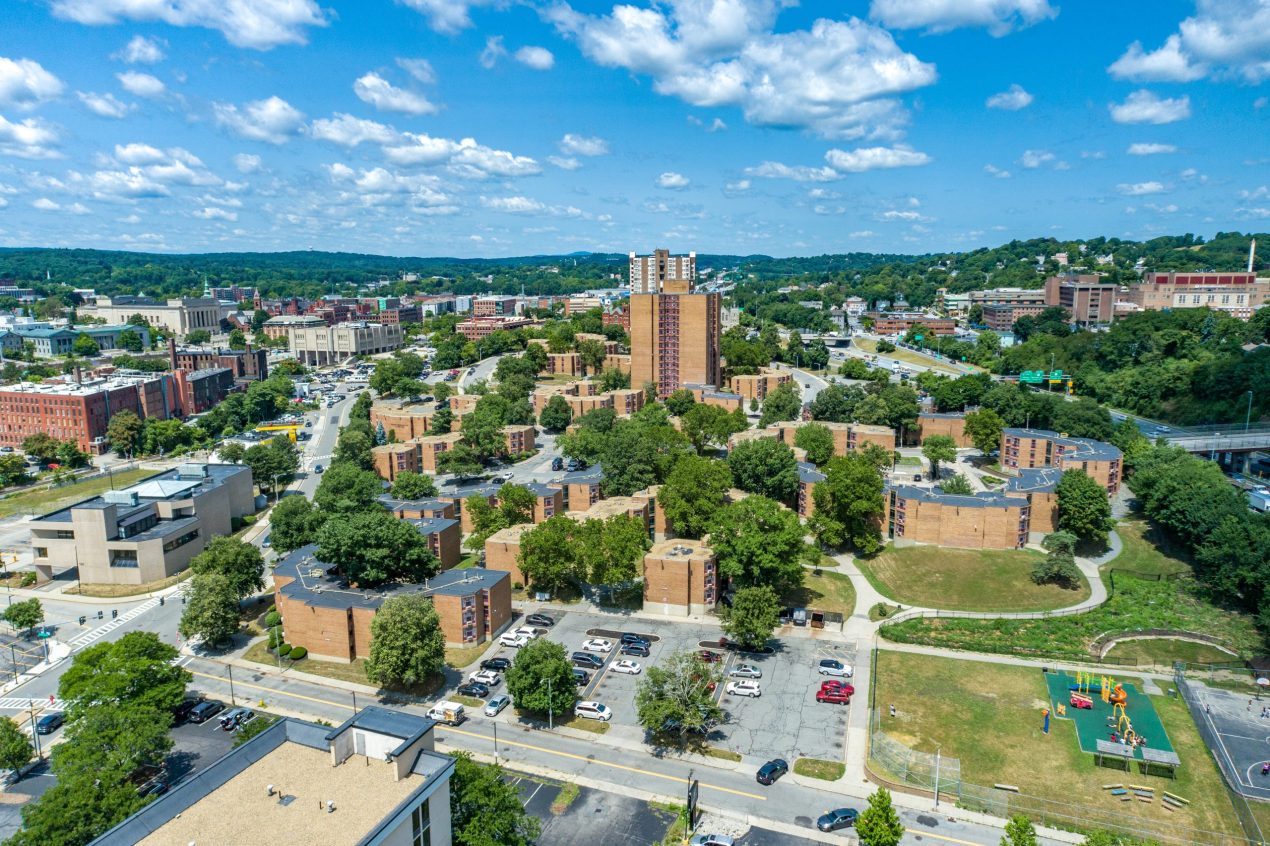 Aerial view of a affordable housing community featuring brick, low-rise apartment buildings with a cityscape behind