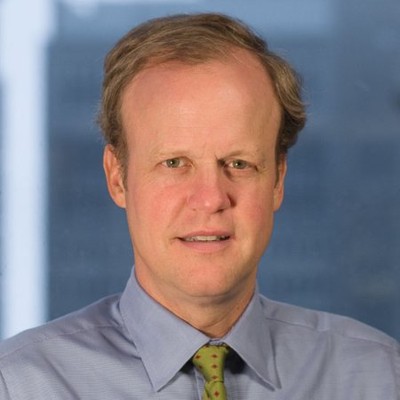 A man with blonde hair wears a blue button down and green tie.