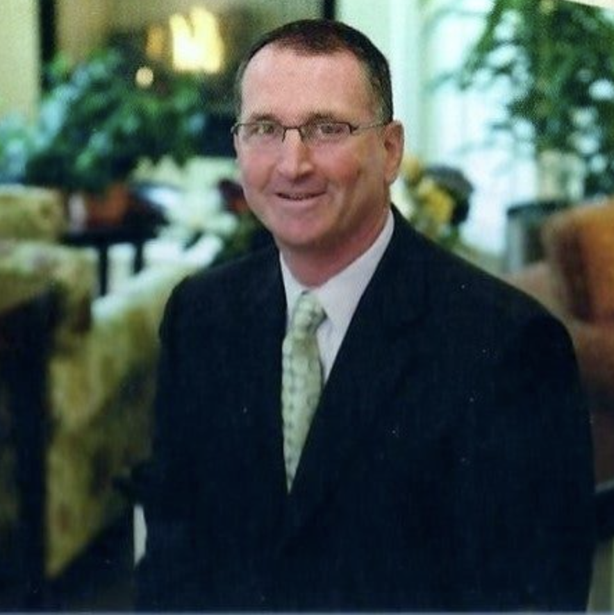 Headshot of a man wearing a black suit jacket and a light green tie