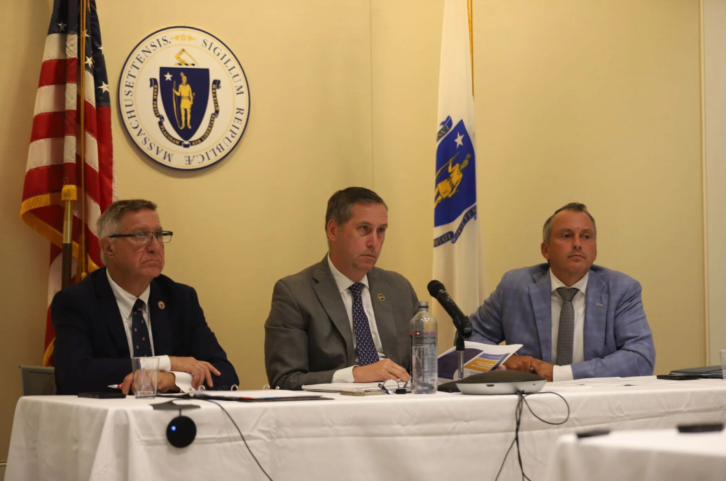 Three men in suits sit a panel during a hearing