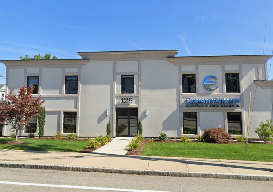 A two-story stucco industrial building's front door sits behind a small lawn and sidewalk.