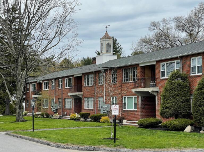 A two-story brick apartment building sits behind a small grass lawn