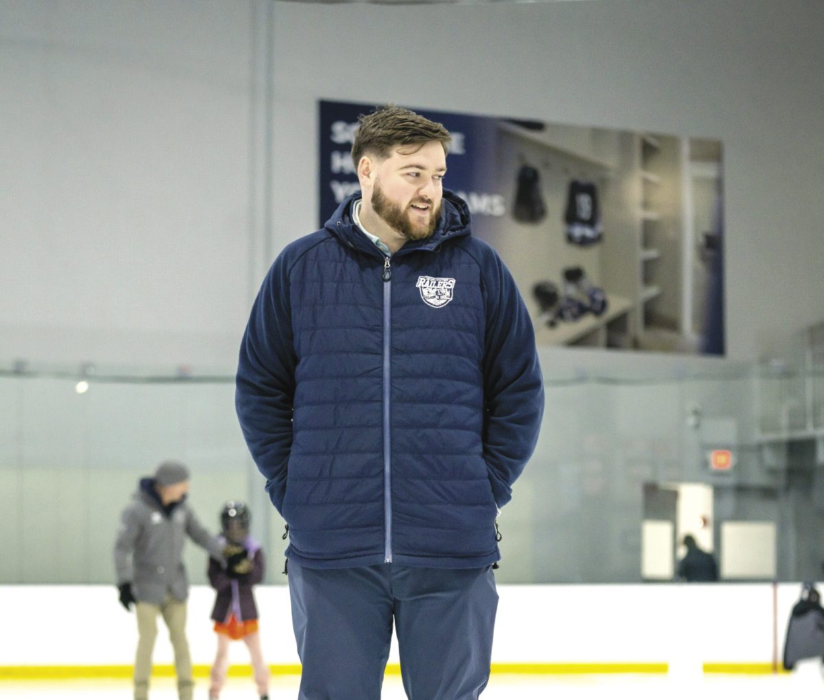 A man wears a blue puffer jacket while standing in an ice rink.