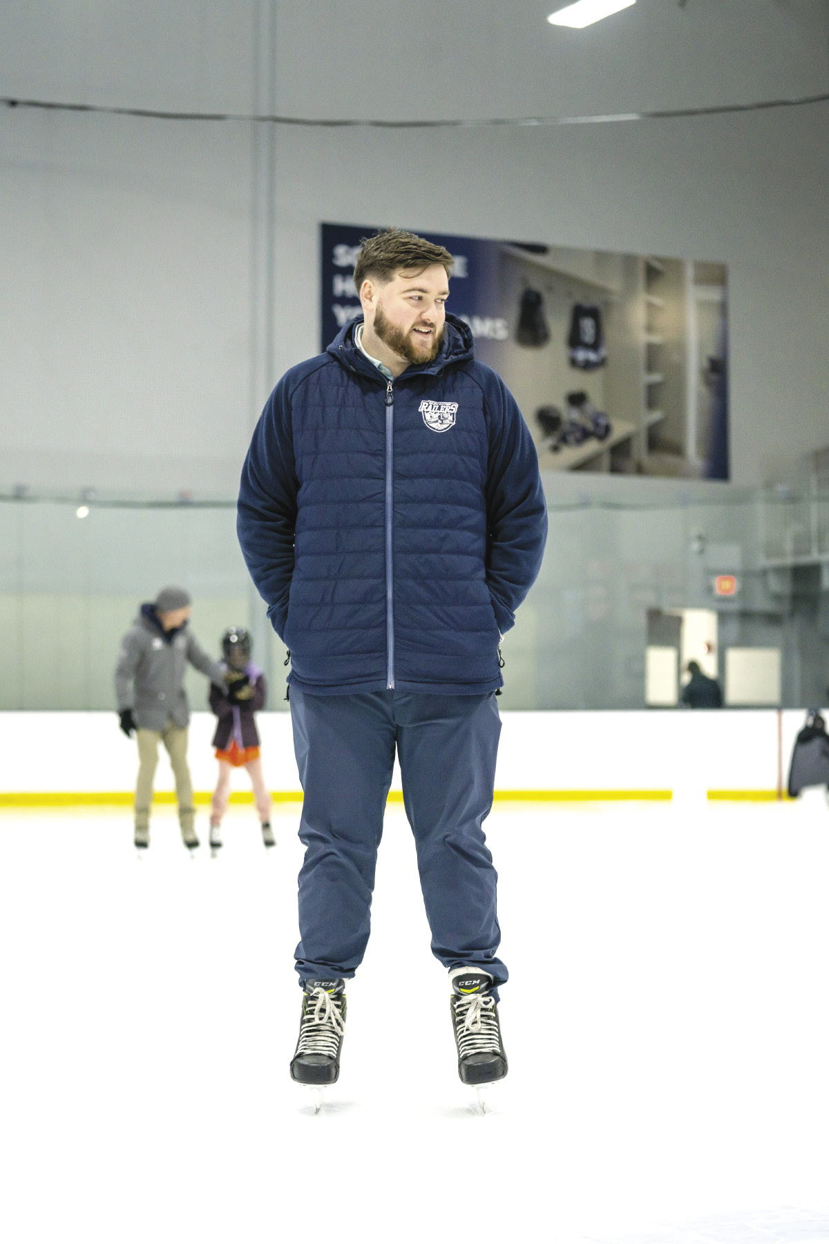 A man wears a blue puffer jacket while standing in an ice rink.