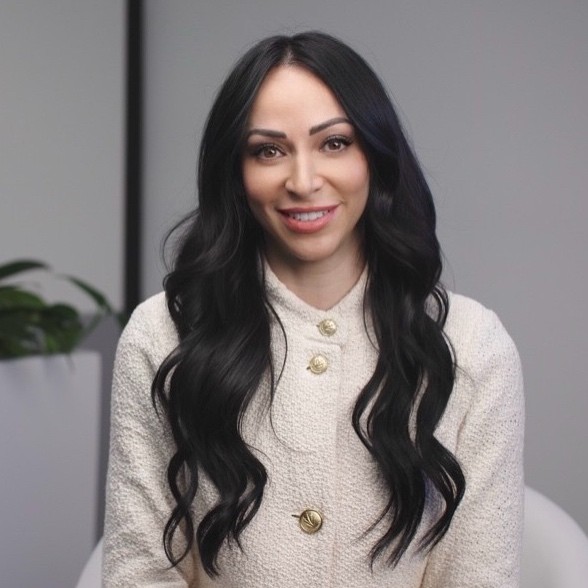 A woman with long, wavy black hair wears a white tweed tacket.