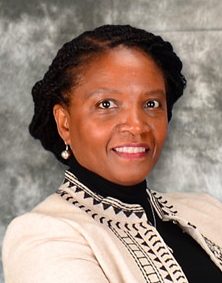 A headshot of a woman wearing a black turtle neck and a white and black jacket