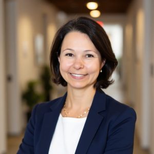 A woman with a brunette bob wears a blue suit jacket and white top.