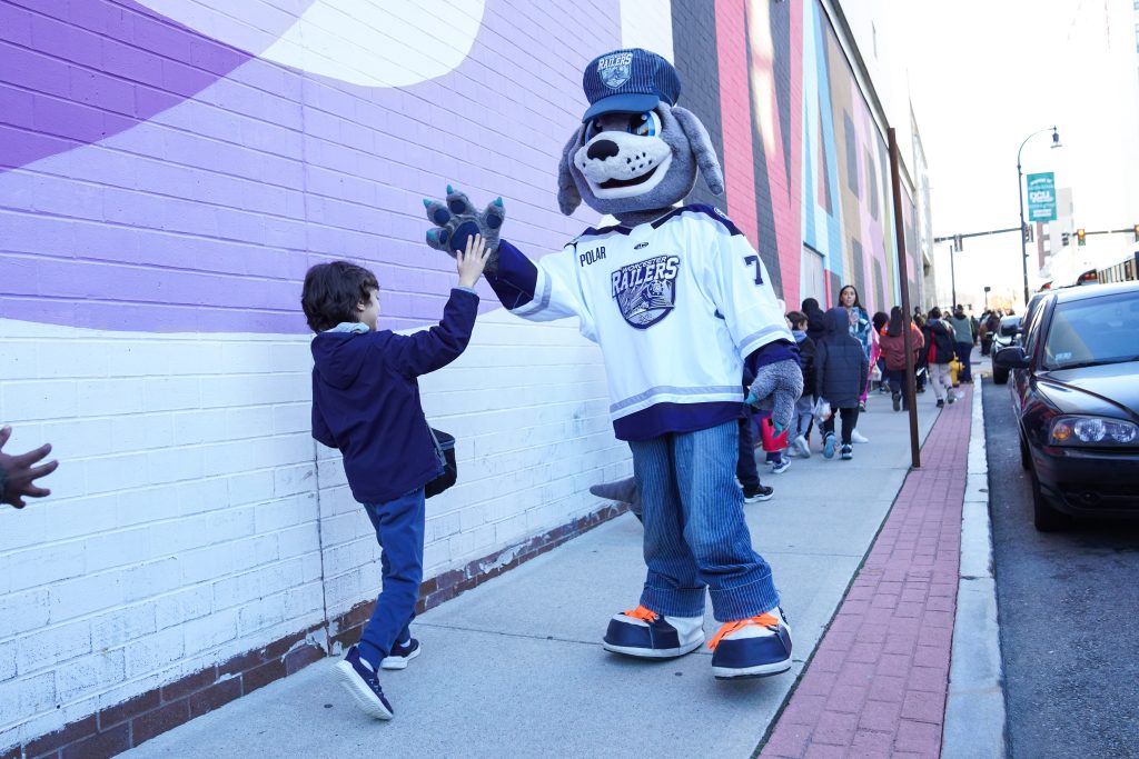 A dog mascot in a train conductor hat and hockey jersey high fives a child