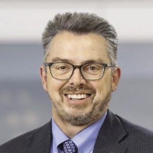 A man with grey and white hair wears glasses.
