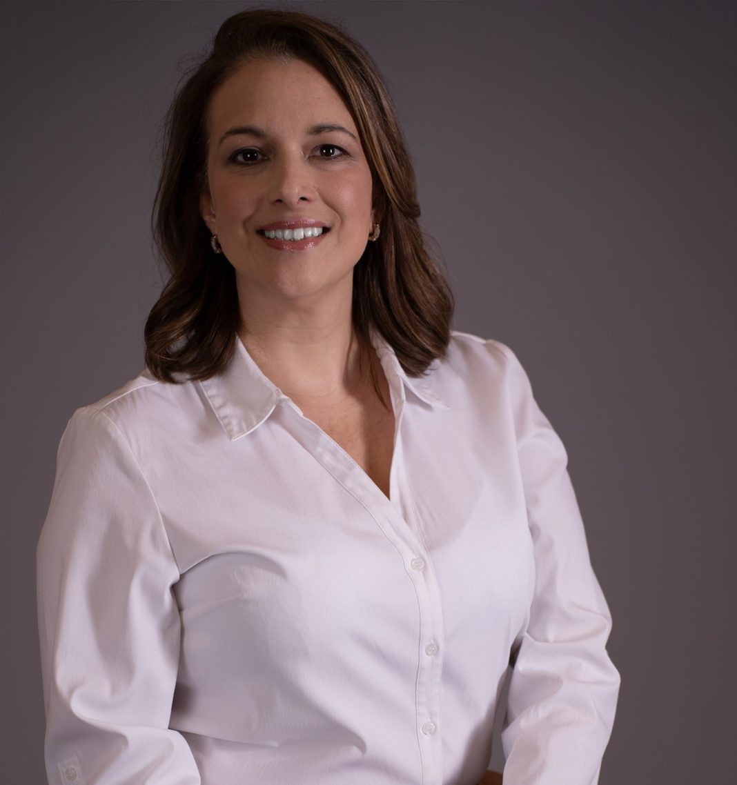 A woman with shoulder-length, light brown hair wears a white button down top.