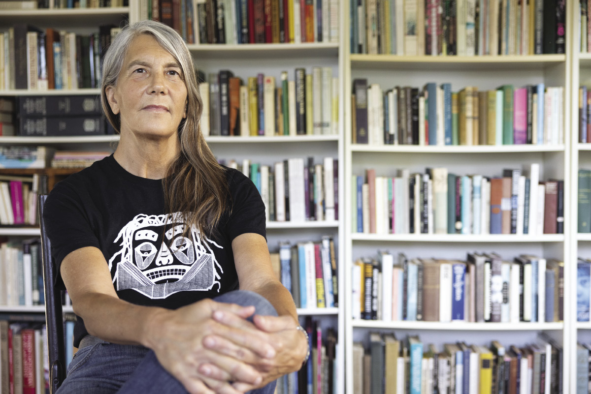 A woman sits in front of a wall of books.