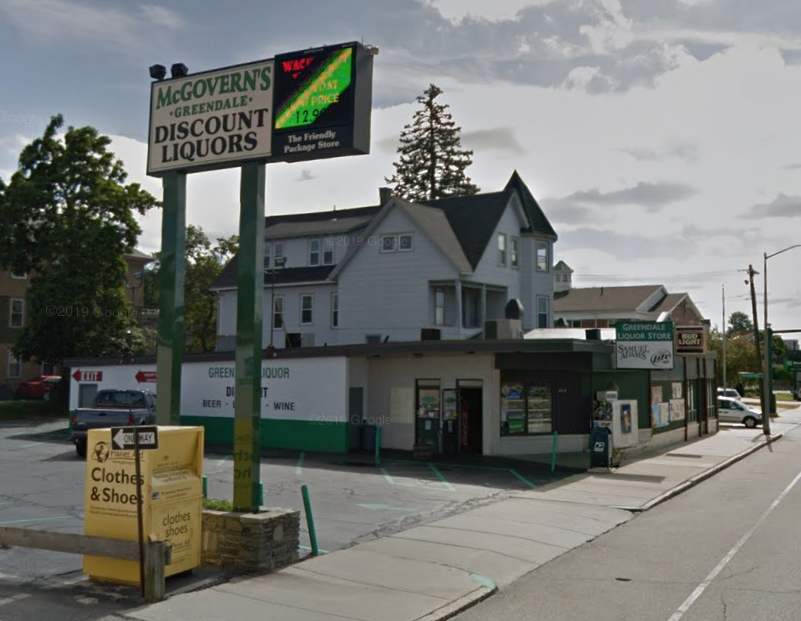 A small liquor store with parking lot and sign out front