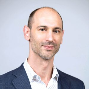 A man wears a dark blue blazer and a white button down.