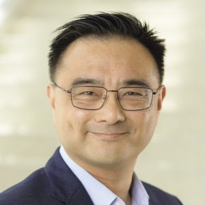 Photo of a dark-haired man wearing thin, black, metal-rimmed glasses.