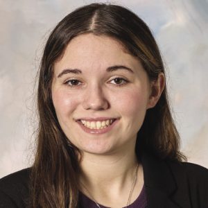 A headshot of a woman with long brown hair parted down the center