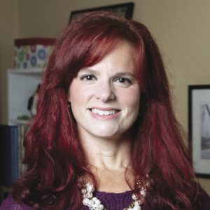 A headshot of a woman with red hair wearing a purple shirt