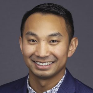 A headshot of a man with short dark hair wearing a dark blue suit jacket