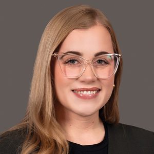 A woman with long blonde hair wears clear cat eye glasses and a black top.