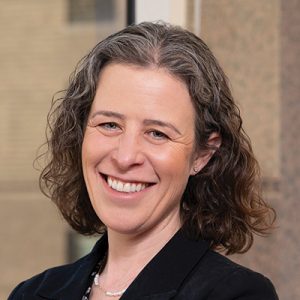 A headshot of a woman with wavy hair wearing a black blazer