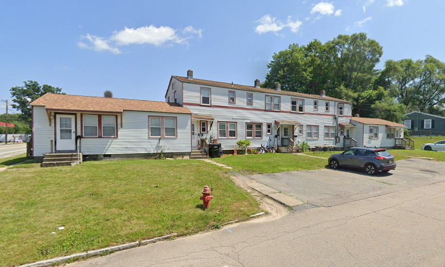 A white townhouse-style building with parking spots and a lawn in front.